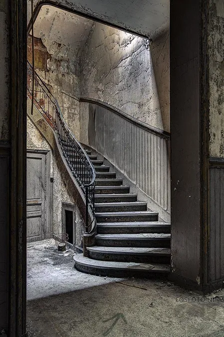 Geschwungene Steintreppe mit abblätternden Wänden und dunklem Geländer.