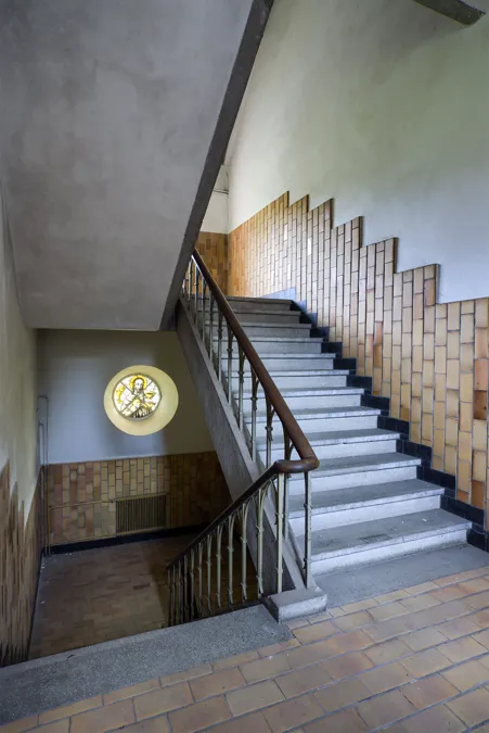 Escalera de hormigón con barandilla metálica, ventana redonda y azulejos escalonados.