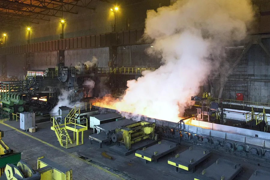 Grand nuage de vapeur blanche au-dessus d’acier incandescent derrière des protections jaunes.