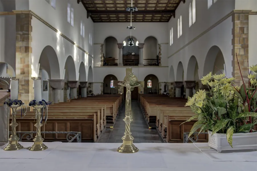 Vista desde el altar sobre los bancos, con cruz de latón y flores delante.