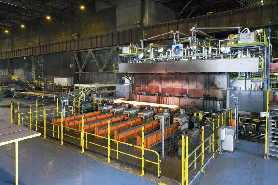 Vue de face d’un grand four industriel et de rouleaux derrière des barrières jaunes.