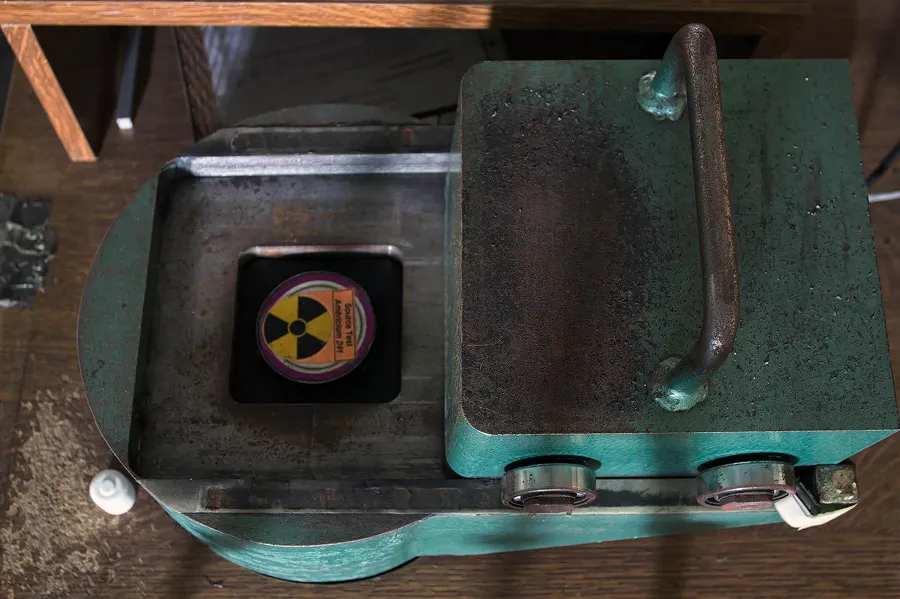 Groene metalen behuizing met open deksel en stralingssymbool.
