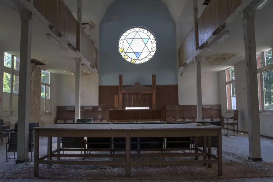 Vista amplia de muros deteriorados de sinagoga, bancos de madera y ventana redonda con estrella.
