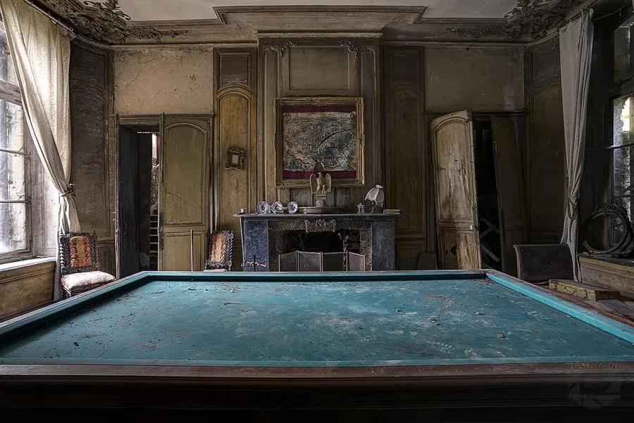 Green billiard table before a fireplace and tall windows