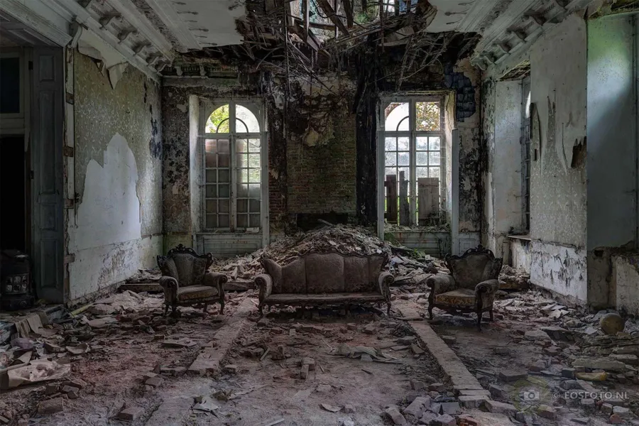 Sofa and armchairs among rubble beneath a badly damaged ceiling