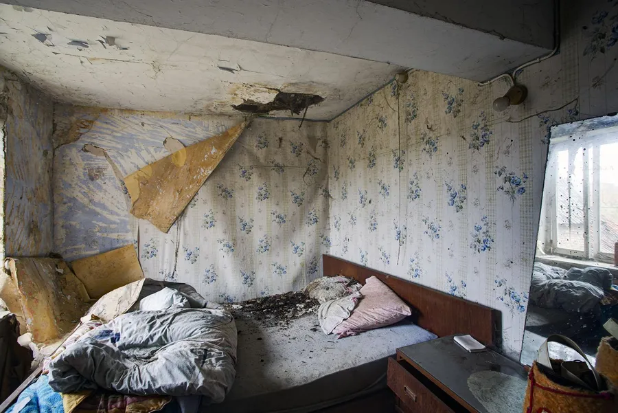 Bett unter beschädigter Decke in einem Zimmer mit Blumentapete