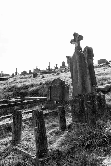 Hohes Grabdenkmal mit Kreuz über verwitterten Steineinfassungen.