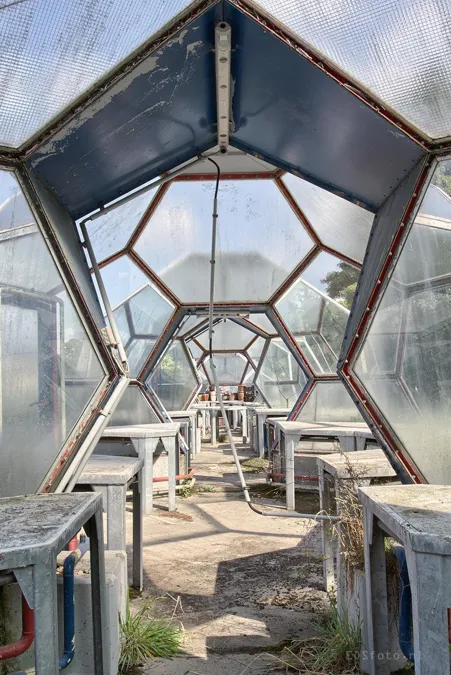 Passage étroit avec tables et grilles de ventilation sous les panneaux du toit de la serre