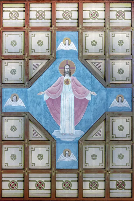 Vista hacia el techo artesonado de madera con una figura central de Cristo sobre fondo azul.
