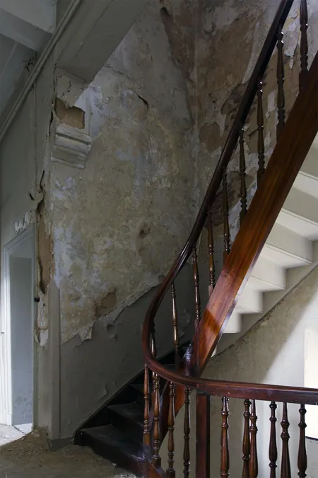 Oude trap met houten leuning langs een beschadigde gepleisterde muur.