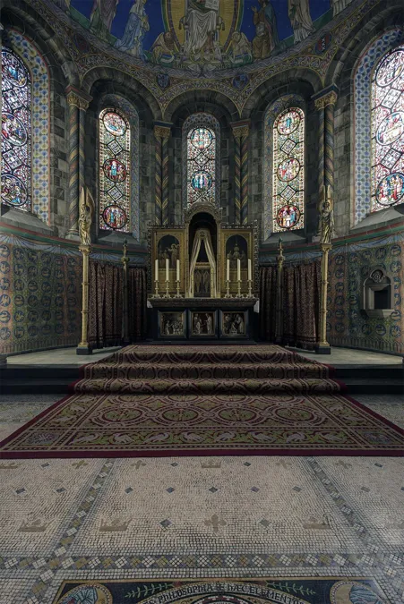 Altar am Ende der Kirche unter Buntglasfenstern und blauen Wandmalereien, mit Teppichen auf dem Boden.