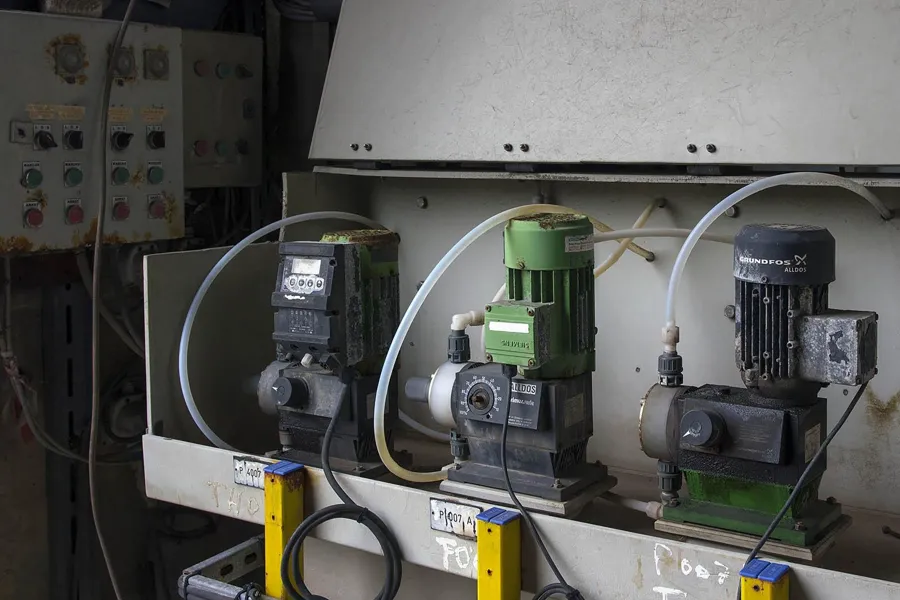 Three pumps with green and black motors before an old control panel.