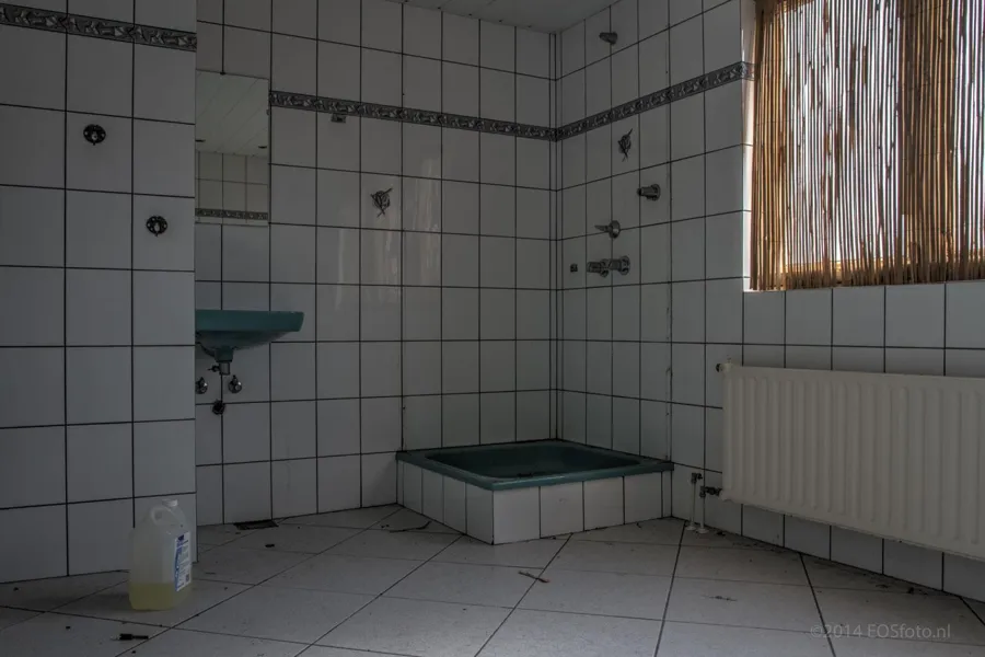 Sala de duchas alicatada con un pediluvio verde bajo.