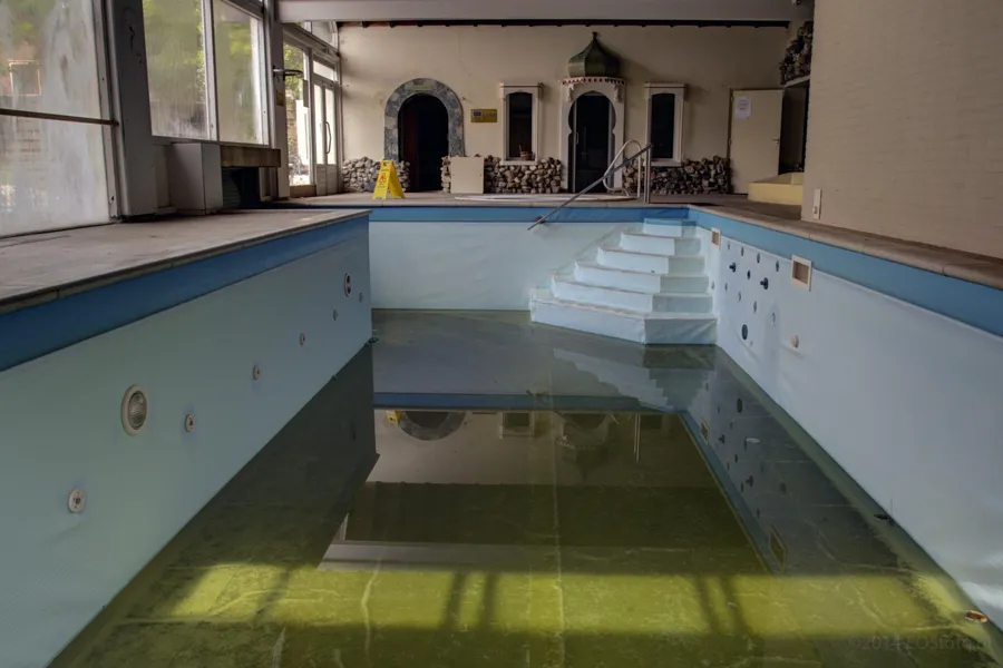 Escalones de la piscina interior vacía con agua verde restante.