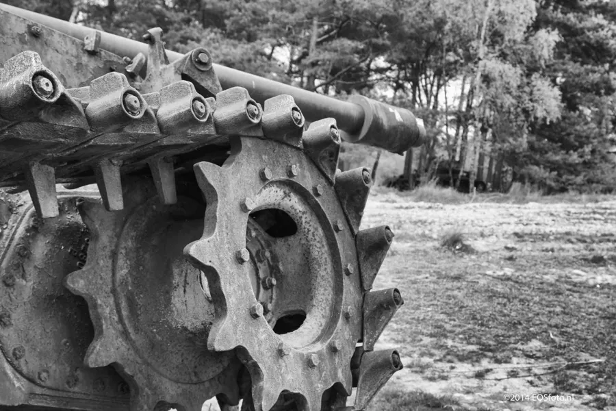 Schwarzweißdetail eines beschädigten Antriebsrads und einer Panzerkette.