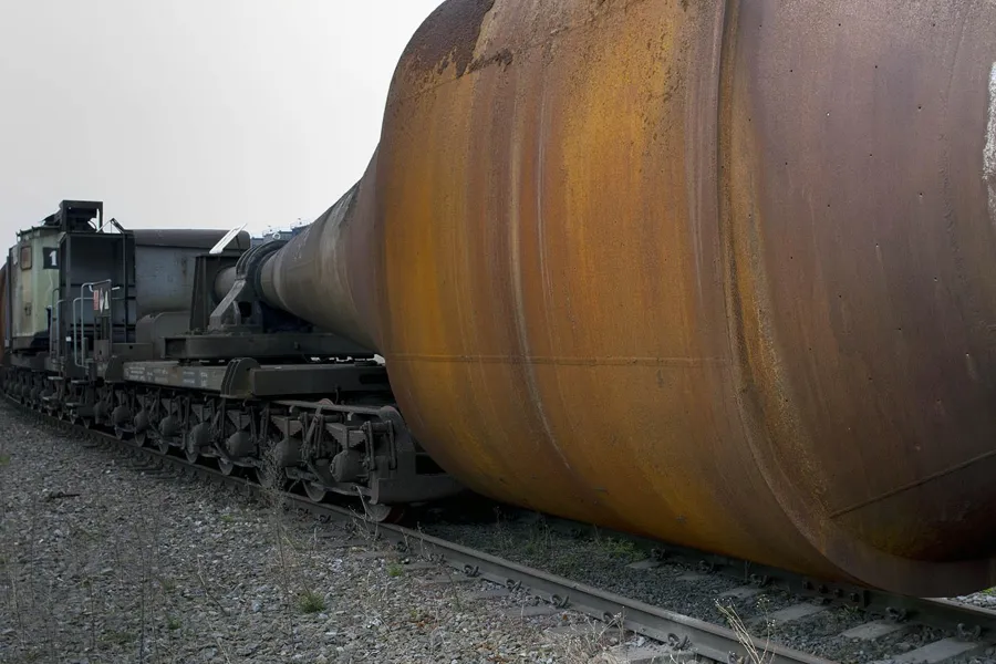 Large rusty bulbous vessel on a chassis with many wheels.