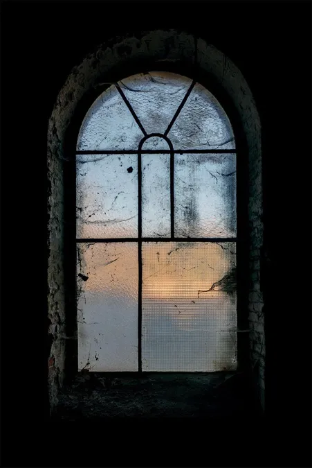Hoog boograam met gekleurd avondlicht achter verweerd glas.