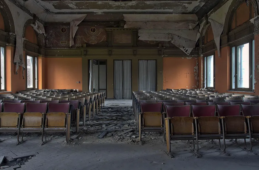 Rows of chairs and ceiling debris in a tall decaying lecture hall.