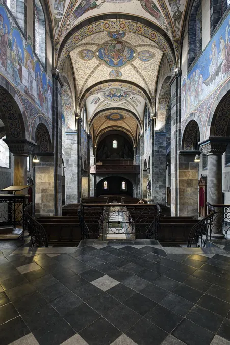 Blick vom Chor zurück durch die Kirche mit dunkler Empore, Säulen und bemalten Gewölben.