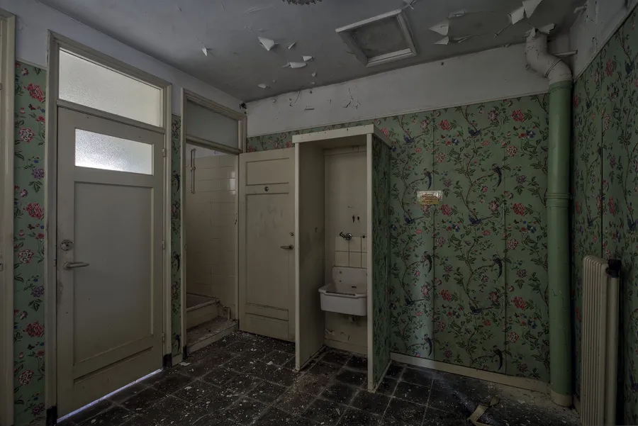 Habitación con papel floral, dos puertas abiertas y lavabo pequeño.