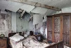 Vue large d'une chambre abîmée avec lit et armoire