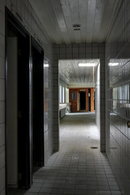 Pasillo oscuro alicatado hacia dos puertas de sauna de madera.