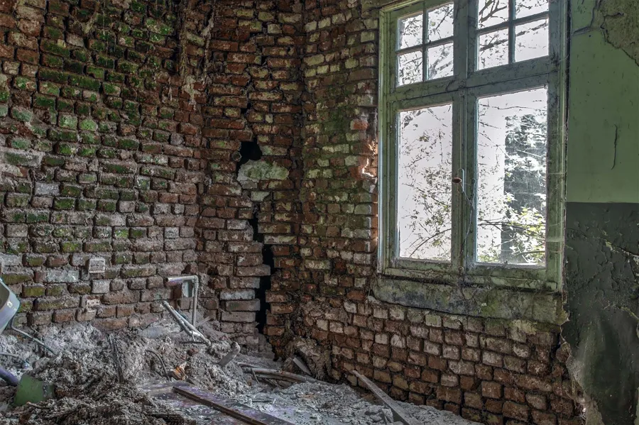 Bare brick wall and rubble beneath a green-framed window.