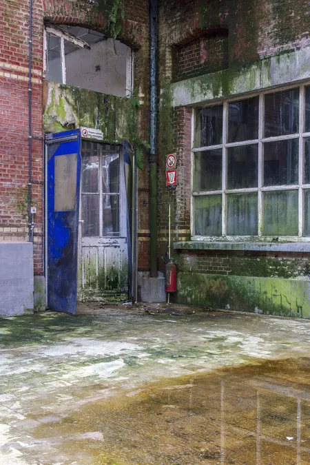 Cour en briques vieillies avec dépôts verts et hautes fenêtres.