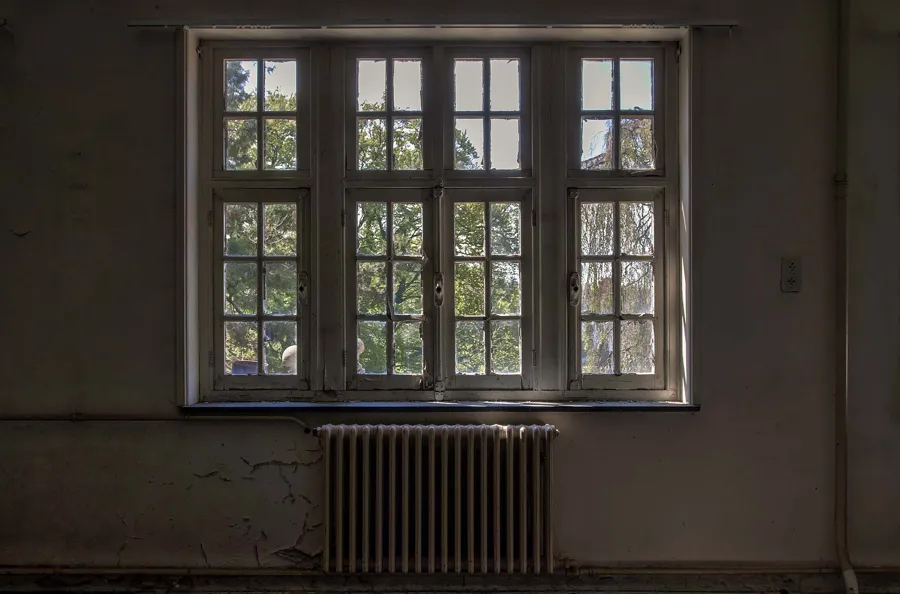 Large fenêtre au cadre écaillé au-dessus d’un radiateur.