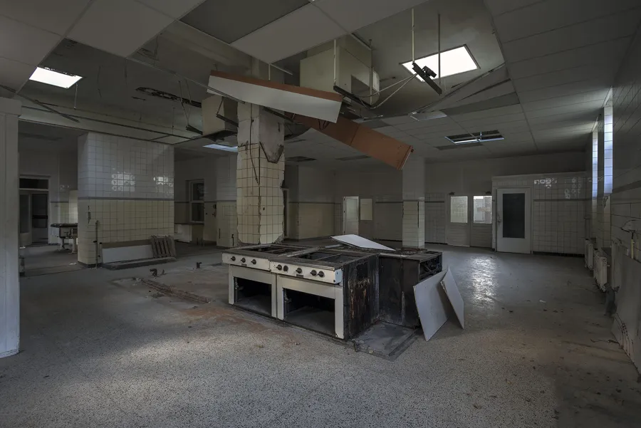 Cocina industrial antigua con isla bajo un falso techo deteriorado.