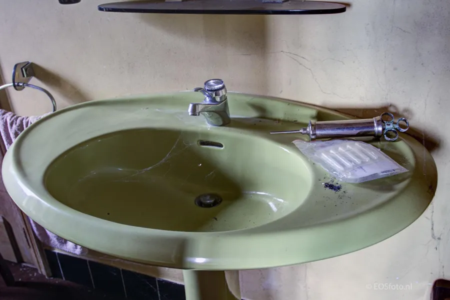 Lavabo verde con grifo y artículos de aseo abandonados