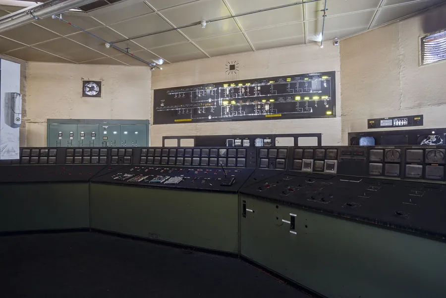 Salle de commande au pupitre vert courbe rempli de cadrans et boutons.