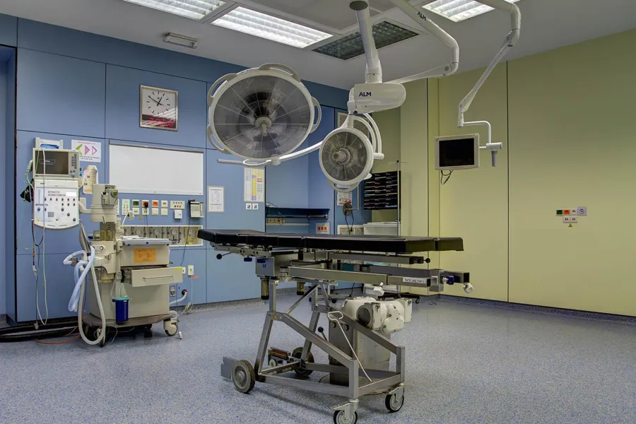 Operating table on a wheeled base in a blue and green operating room.