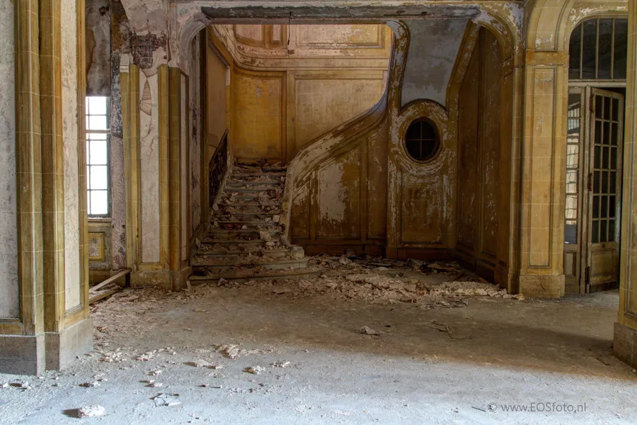 Cage d’escalier ouvragée aux murs jaunes écaillés et à l’ouverture ronde.
