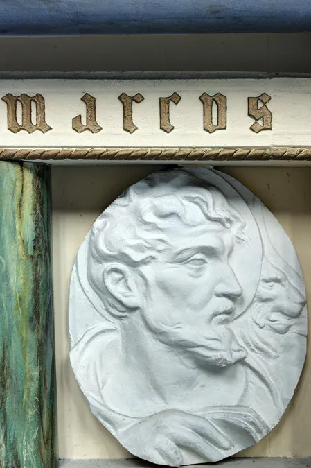 Detalle de relieve blanco con dos cabezas masculinas bajo letras doradas.