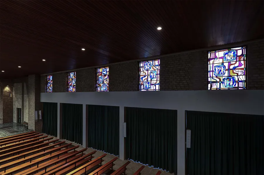 Row of small stained-glass windows above dark green curtains and empty pews.
