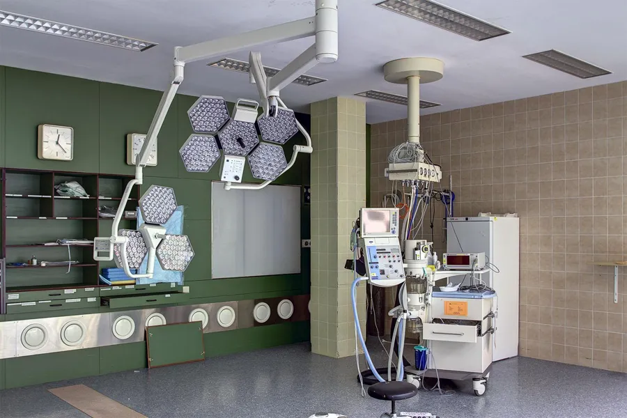 Multi-section surgical lights beside a medical machine in an empty room.