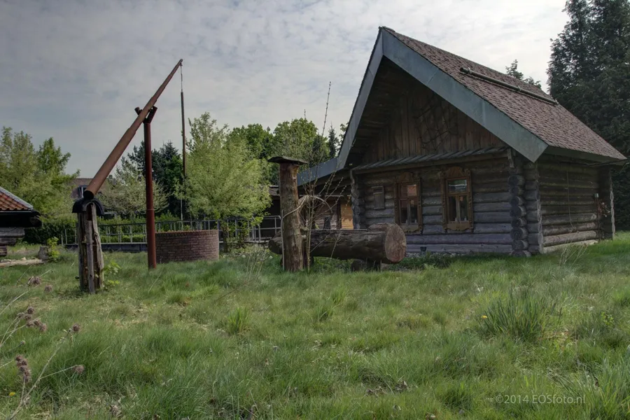 Cabaña de sauna de madera con tejado a dos aguas en un jardín descuidado.