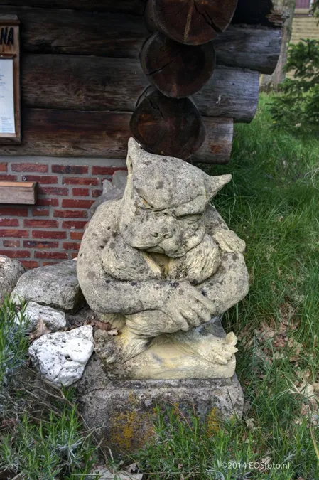 Estatua pequeña deteriorada junto a la base de ladrillo de una sauna de madera.
