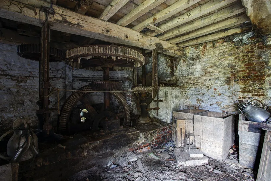 Mühlenmechanik neben Holzkästen und beschädigtem Mauerwerk