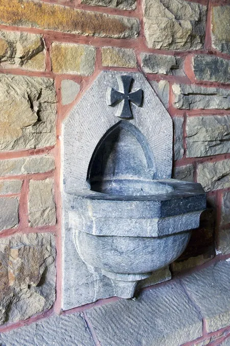 Stenen wijwaterbakje met kruis op een gemetselde muur.