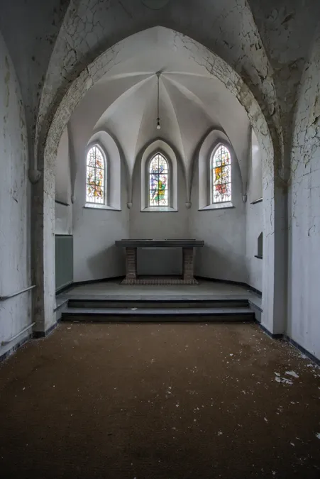 Sala blanca abovedada vacía con techo deteriorado y tres ventanas arqueadas.