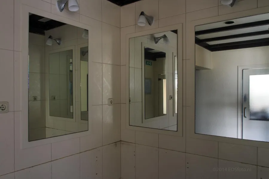 Tres espejos de pared con luces en una esquina alicatada.