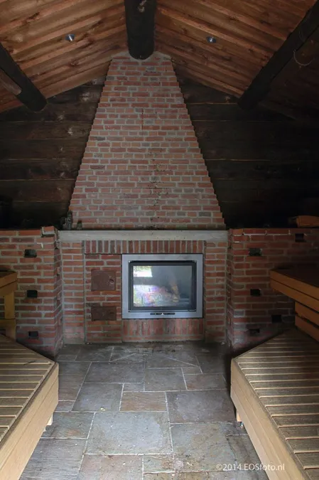Chimenea de ladrillo entre bancos de madera bajo un tejado a dos aguas.