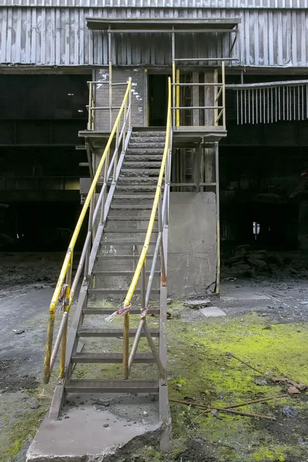 Narrow steel staircase with yellow railings leading to a high platform.
