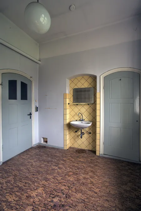 Habitación blanca pequeña con dos puertas grises y lavabo en nicho.