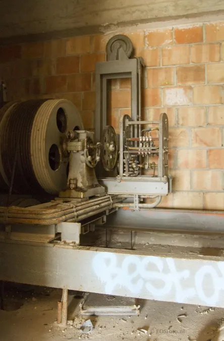 Alte Maschine mit großem Rad auf einem Metallgestell in einem Backsteinraum.