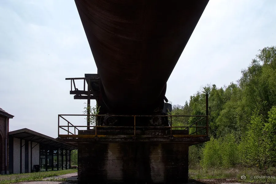 Lange roestige oven boven een betonnen steun met metalen bordes.