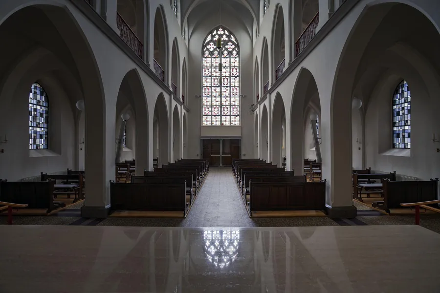 Zicht vanaf het altaar door de kapel naar een hoog raam boven de achterste banken.