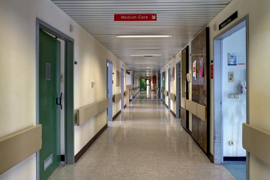 Long hospital corridor with green doors and a Medium-Care sign.